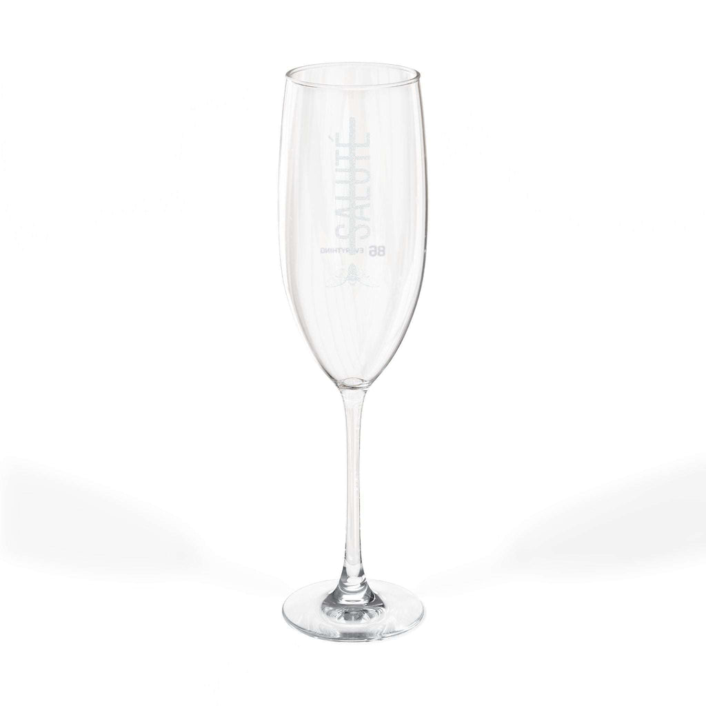 Single clear glass champagne flute with SALUTÉ and 86 EVERYTHING printed on the side.